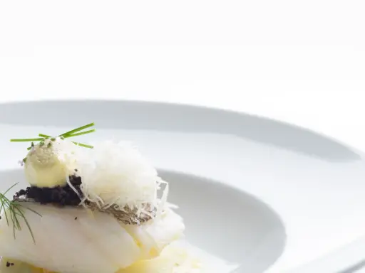 Piatto gourmet con filetto di pesce bianco, crema gialla, erbe aromatiche e fili croccanti. Un'interpretazione moderna che evoca la differenza tra baccalà e stoccafisso.