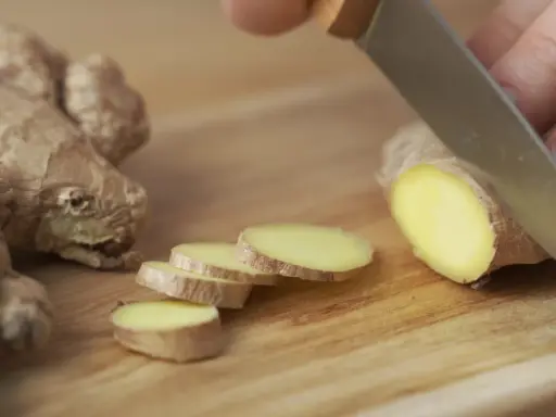 Un pezzo di zenzero fresco viene affettato su un tagliere di legno, mostrando come si mangia questo ingrediente versatile.