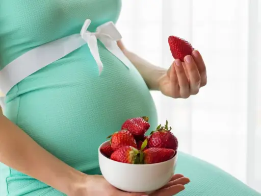 Pancione e fragole, un dolce desiderio in gravidanza. La futura mamma tiene una fragola in mano e una ciotola piena.