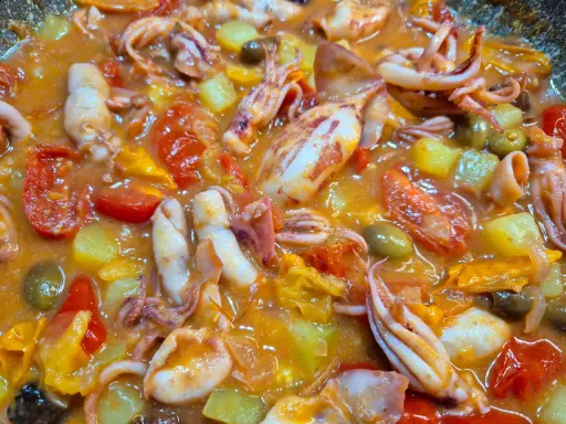Totani in umido con pomodoro, patate e olive, un piatto saporito e colorato, pronto per essere gustato.
