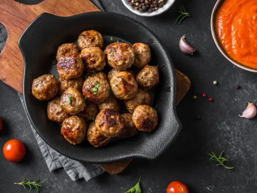 Polpette dorate e succulente, appena sfornate dalla friggitrice ad aria, pronte per essere gustate con salsa e pomodorini freschi.