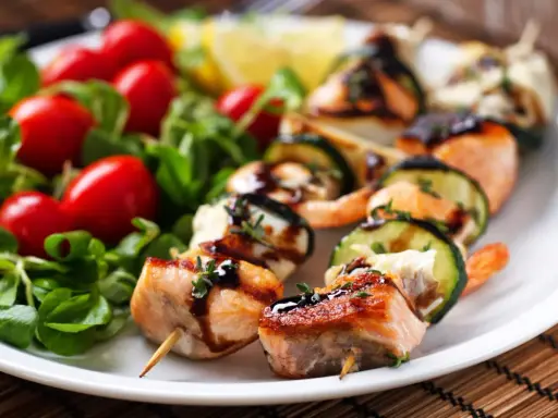 Spiedini di pesce succulenti con salmone, gamberi e zucchine, guarniti con erbe aromatiche e salsa, serviti con insalata fresca e pomodorini.