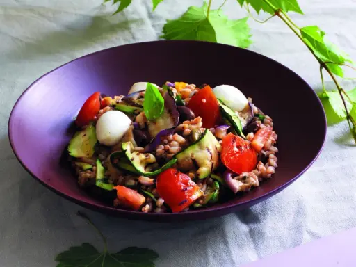 Insalata di farro estiva con verdure grigliate, pomodorini, mozzarelline e basilico, un piatto fresco e colorato.