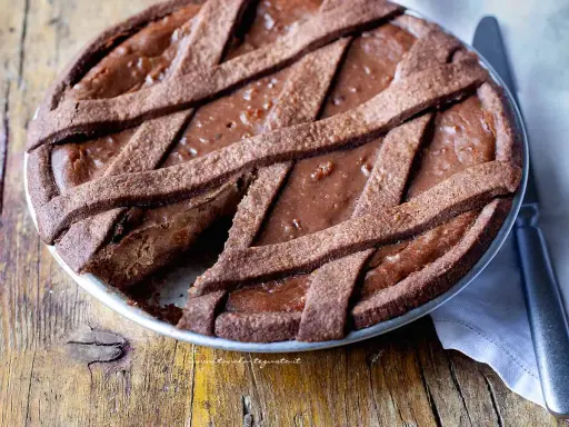 Pastiera al cioccolato con scorze candite, un dolce goloso su un tavolo di legno rustico.