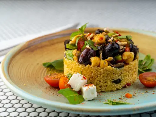 Cous cous condito con olive, ceci, pomodorini e feta. Un'idea gustosa su come condire il cous cous per un piatto colorato e saporito.