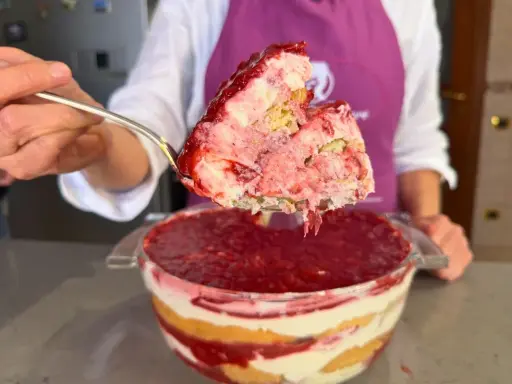 Un cucchiaio solleva una porzione generosa di un goloso tiramisù alle fragole, stratificato con crema e biscotti, pronto per essere gustato.