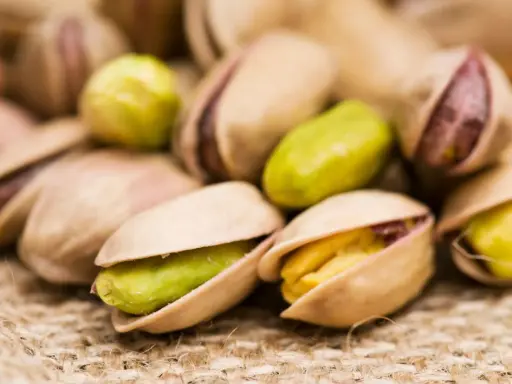 Un mucchio di pistacchi, alcuni aperti rivelano il loro interno verde e giallo. Attenzione, i pistacchi fanno ingrassare!