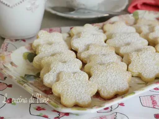 Deliziosi biscotti al burro a forma di fiore, spolverati di zucchero a velo, su un vassoio floreale.