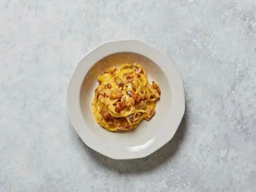 Un piatto di spaghetti alla carbonara, con il suo guanciale croccante e la crema d'uovo e pecorino, pronto per essere gustato.