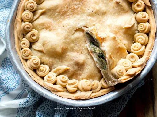 Torta salata con carciofi, decorata con rose di pasta frolla e foglie, pronta per essere gustata.