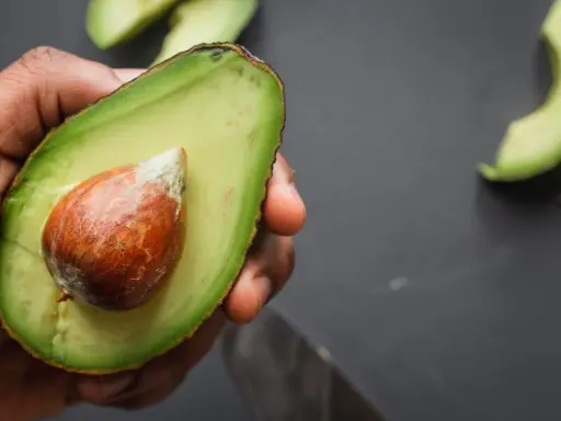 Mano che tiene mezzo avocado maturo con nocciolo. Ecco come si mangia l'avocado: fresco, spalmato o in insalata.