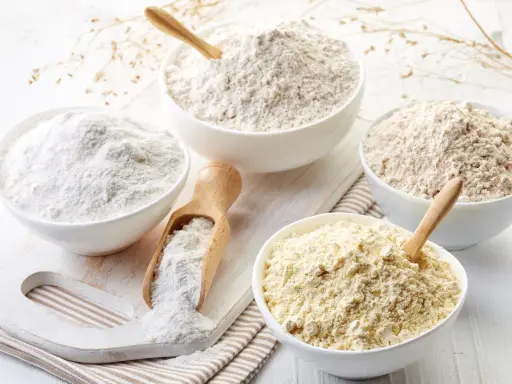 Diverse ciotole mostrano vari tipi di farina, da quella bianca finissima a quelle più grezze e giallastre, pronte per ogni ricetta.