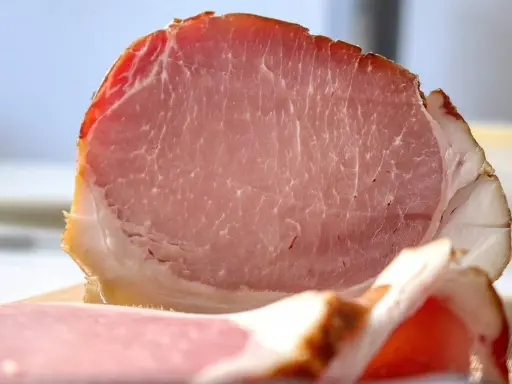 Fetta di prosciutto cotto, un insaccato rosa con striature di grasso bianco e un bordo dorato.