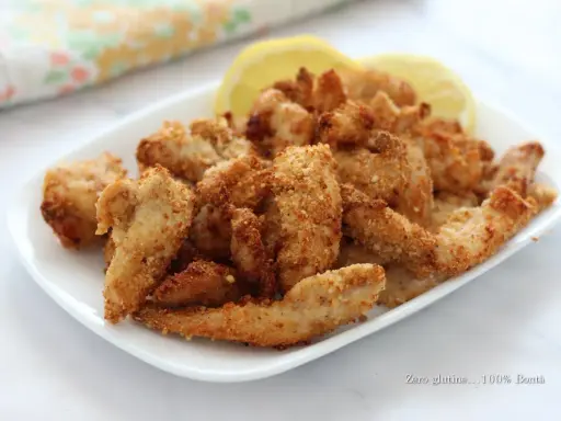 Straccetti di pollo croccanti in friggitrice ad aria, serviti con spicchi di limone.