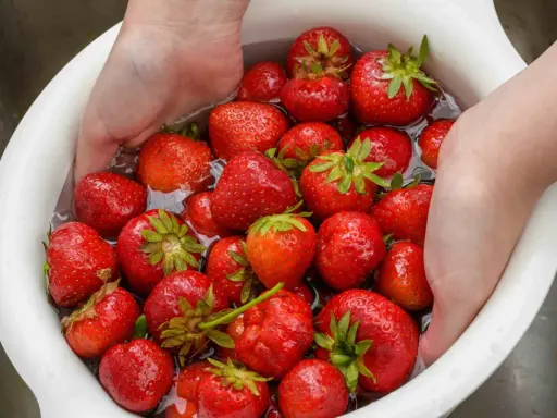Mani che lavano fragole rosse in una ciotola bianca piena d'acqua. Un modo semplice per preparare questo frutto delizioso.