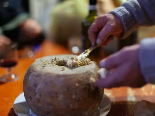 Un uomo serve un formaggio con i vermi, una specialità sarda, con un coltello. Sul tavolo, un bicchiere di vino rosso.