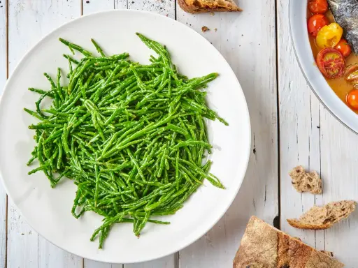 Piatto bianco colmo di asparagi di mare freschi e croccanti, pronti per essere gustati.