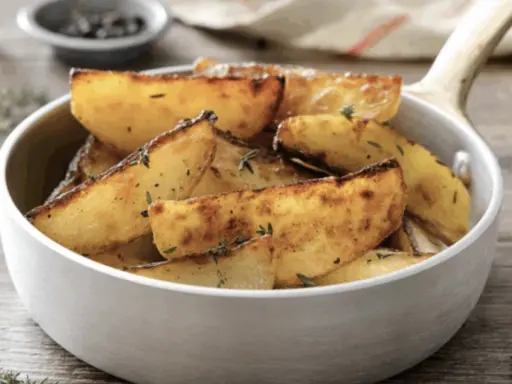 Patate in padella dorate e croccanti, condite con erbe aromatiche, servite in una ciotola bianca.