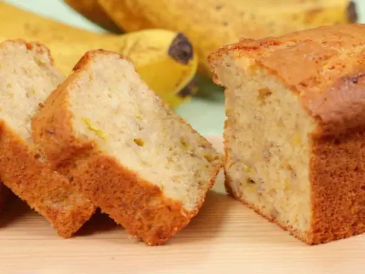 Fette di banana bread light, soffice e dorato, con banane mature sullo sfondo.