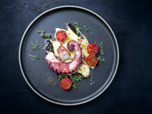 Un tentacolo di polpo alla griglia, servito su purè di patate con pomodorini confit e timo.