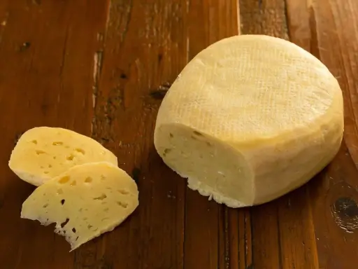 Formaggio di fossa, un sapore antico. Un pezzo di formaggio stagionato e due fette su un tavolo di legno rustico.