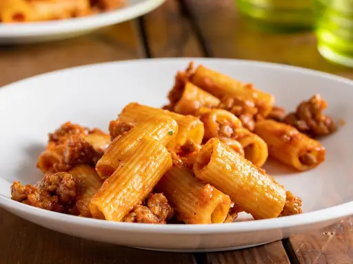 Rigatoni conditi con un ricco ragù di salsiccia alla napoletana, serviti su un piatto bianco.