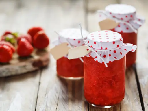 Barattoli di marmellata di fragole fatti in casa, con fragole fresche sullo sfondo.