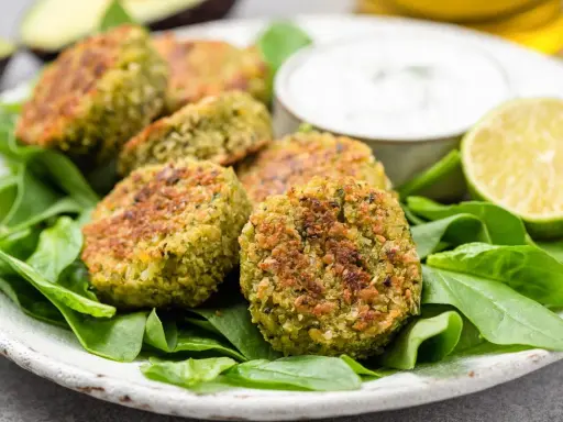 Polpette di spinaci dorate su un letto di spinaci freschi, con una ciotolina di salsa e spicchi di lime.