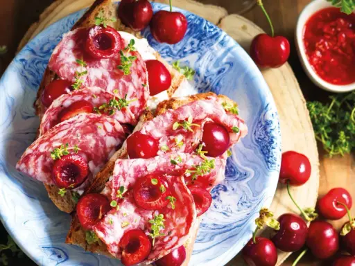 Bruschette con salame e varietà ciliegie giganti, guarnite con erbe aromatiche. Un connubio di sapori audace e invitante.
