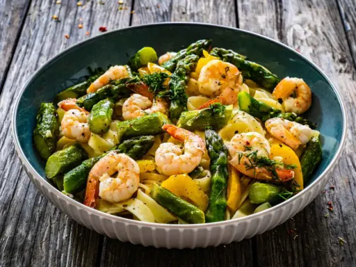 Un piatto invitante di pasta con asparagi e gamberetti, condito con erbe fresche e servito su un tavolo di legno rustico.