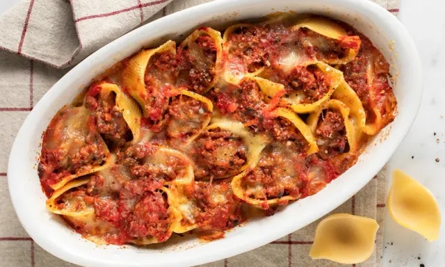 Conchiglioni ripieni al forno, un piatto invitante con pasta ripiena di carne, salsa di pomodoro e formaggio fuso, pronto per essere gustato.