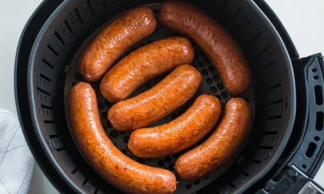 Sette salsicce dorate e succulente cuociono nella friggitrice ad aria, pronte per essere gustate.