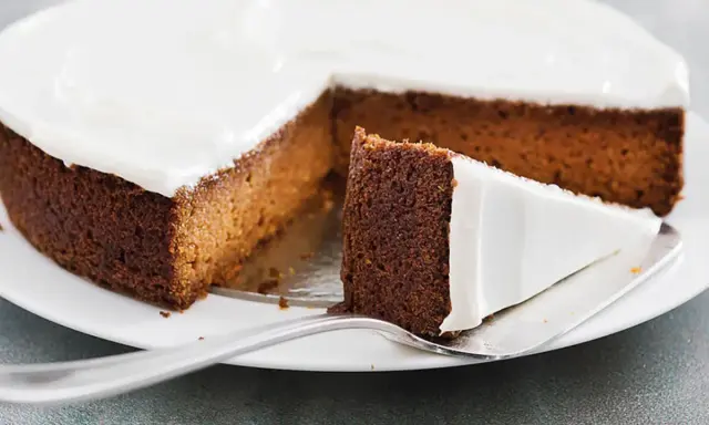 Una fetta di torta di carote e yogurt, soffice e ricoperta di glassa bianca, pronta per essere gustata.