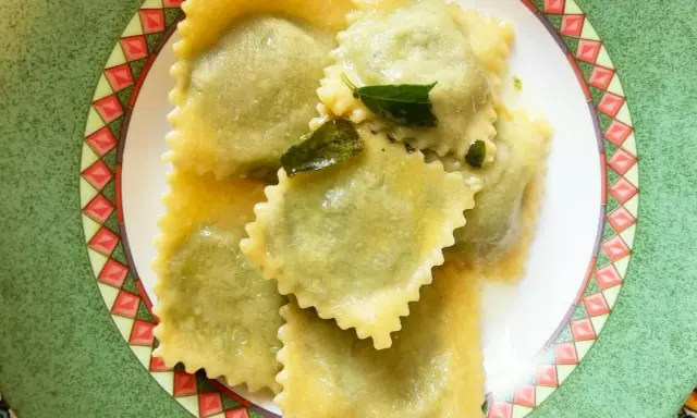 Ravioli ricotta e spinaci conditi con burro fuso e salvia, serviti su un piatto decorato.