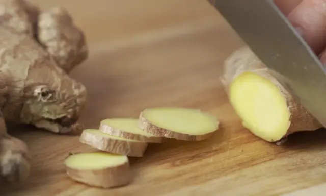 Un pezzo di zenzero fresco viene affettato su un tagliere di legno, mostrando come si mangia questo ingrediente versatile.