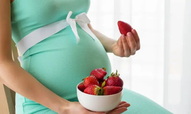 Pancione e fragole, un dolce desiderio in gravidanza. La futura mamma tiene una fragola in mano e una ciotola piena.