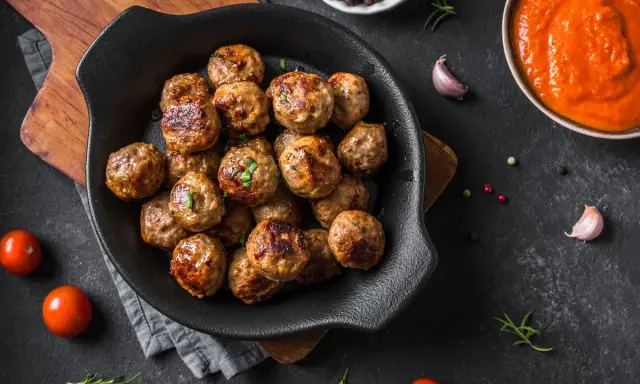 Polpette dorate e succulente, appena sfornate dalla friggitrice ad aria, pronte per essere gustate con salsa e pomodorini freschi.