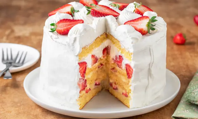 Torta fragole e panna, soffice pan di Spagna farcito con panna montata e tante fragole fresche, decorata con fragole a fette e ciuffi di panna.