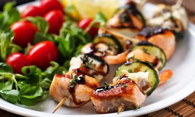 Spiedini di pesce succulenti con salmone, gamberi e zucchine, guarniti con erbe aromatiche e salsa, serviti con insalata fresca e pomodorini.