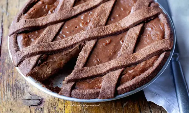 Pastiera al cioccolato con scorze candite, un dolce goloso su un tavolo di legno rustico.