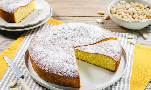 Una deliziosa torta con farina di mandorle, spolverata di zucchero a velo, pronta per essere gustata. Accanto, una ciotola di mandorle intere.