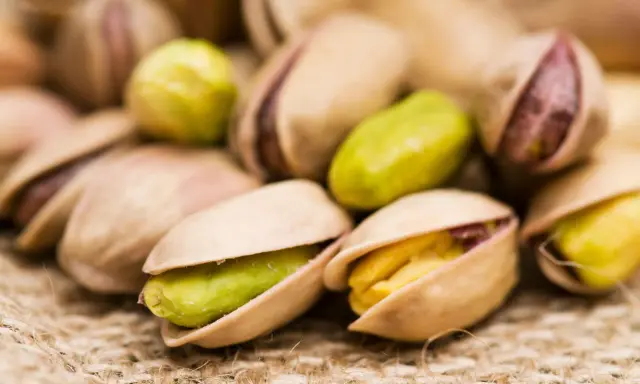Un mucchio di pistacchi, alcuni aperti rivelano il loro interno verde e giallo. Attenzione, i pistacchi fanno ingrassare!