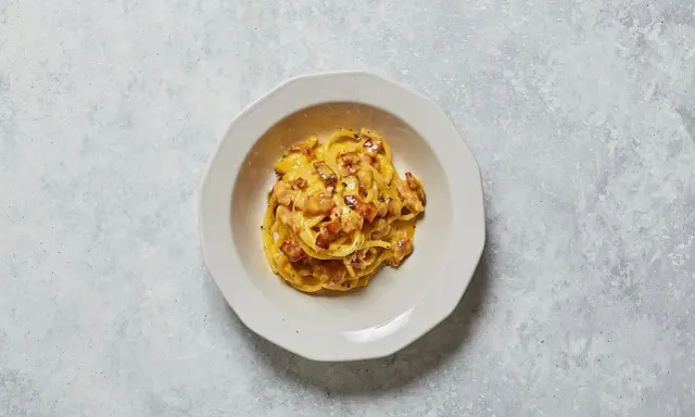 Un piatto di spaghetti alla carbonara, con il suo guanciale croccante e la crema d'uovo e pecorino, pronto per essere gustato.