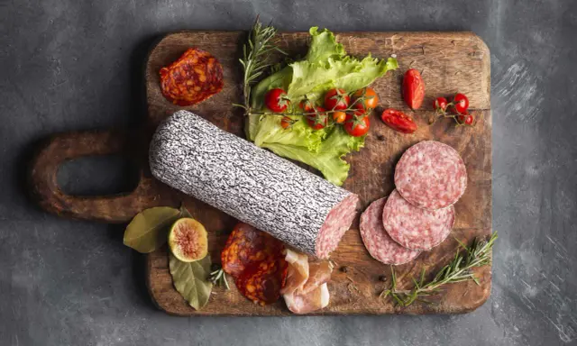 Assortimento di tipi di salame su tagliere in legno, con pomodorini, lattuga e fichi.