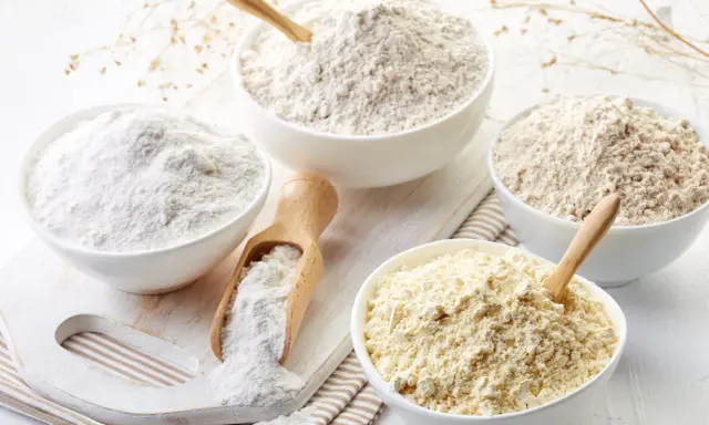 Diverse ciotole mostrano vari tipi di farina, da quella bianca finissima a quelle più grezze e giallastre, pronte per ogni ricetta.