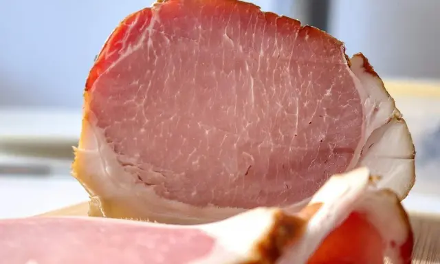 Fetta di prosciutto cotto, un insaccato rosa con striature di grasso bianco e un bordo dorato.