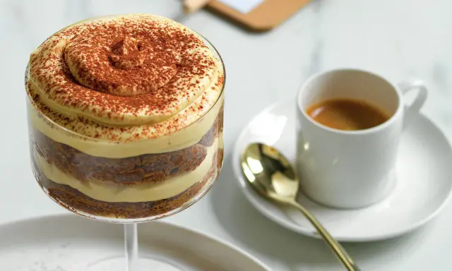 Delizioso tiramisù senza caffè, stratificato con crema e cacao, accanto a un espresso.