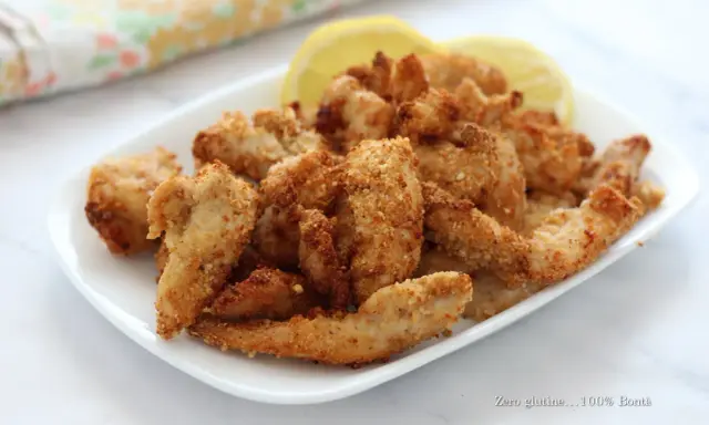 Straccetti di pollo croccanti in friggitrice ad aria, serviti con spicchi di limone.