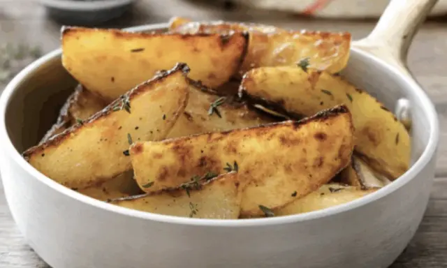 Patate in padella dorate e croccanti, condite con erbe aromatiche, servite in una ciotola bianca.