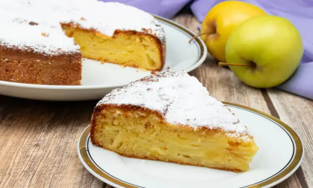 Una fetta di torta di mele invisibile, soffice e profumata, cosparsa di zucchero a velo. Accanto, mele fresche e un tovagliolo viola.